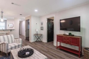 A living room with a striped sofa, a coffee table, a red cabinet, and a TV mounted on the wall. - Newly Renovated, 1st Floor Condo: Walk to Campus! (Oxford)