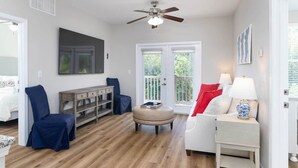 A living room with a ceiling fan, a sofa, a chair, a side table with a lamp, and a wooden cabinet. - A New Luxury Oxford Condo Close to Everything! (Oxford)