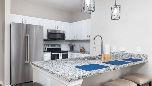 A kitchen with white cabinets, stainless steel appliances, granite countertops, and bar stools. - A New Luxury Oxford Condo Close to Everything! (Oxford)
