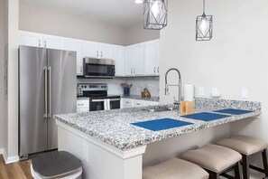 A kitchen with white cabinets, stainless steel appliances, granite countertops, and bar stools. - A New Luxury Oxford Condo Close to Everything! (Oxford)