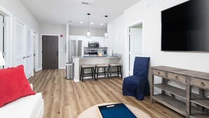 A compact living space with a kitchenette, a flat-screen TV, a dining area, and a seating area with a blue chair. - A New Luxury Oxford Condo Close to Everything! (Oxford)