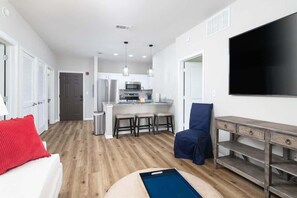 A compact living space with a kitchenette, a flat-screen TV, a dining area, and a seating area with a blue chair. - A New Luxury Oxford Condo Close to Everything! (Oxford)