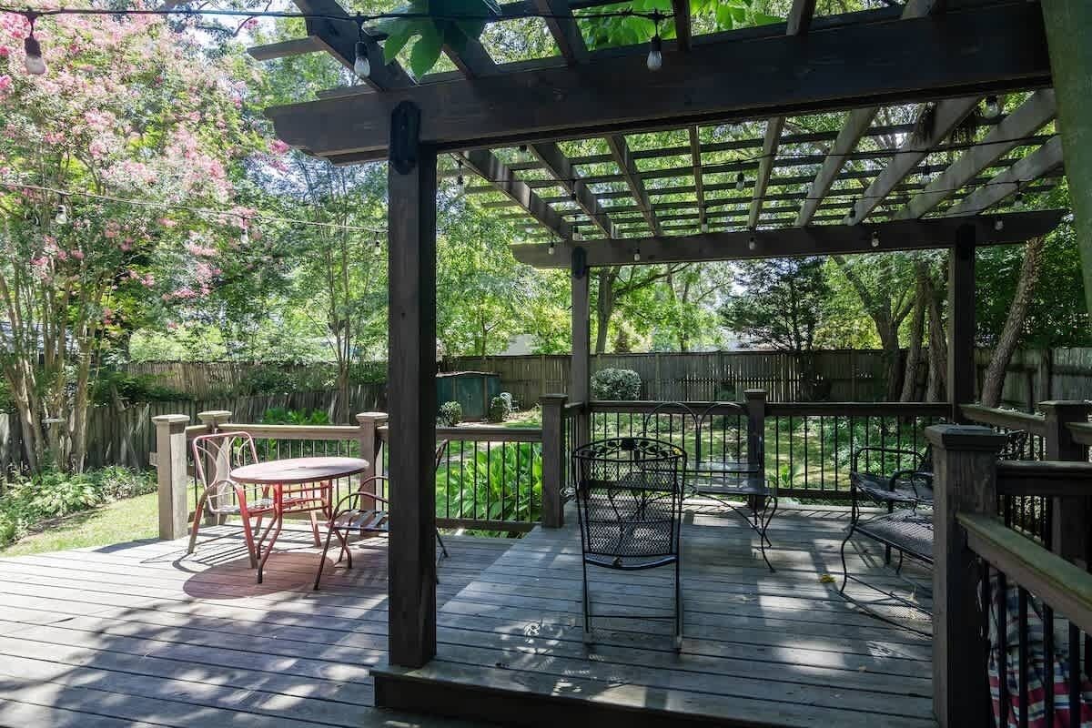 A wooden deck with a pergola, outdoor furniture, and a garden backdrop.