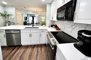A modern kitchen with white cabinetry, a built-in dishwasher, a coffee maker, and a microwave. - Oxford Contemporary Retreat (Oxford)