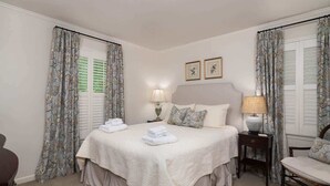 Ein Hotelzimmer mit einem Bett, zwei Nachttischen mit Lampen, einem Sessel und Vorhängen.