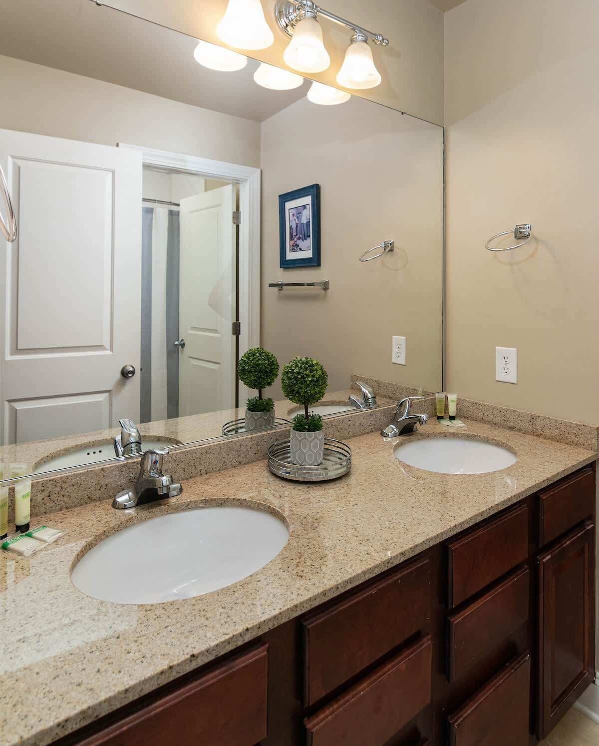 A bathroom with two sinks, a large mirror, and a door leading to another room.