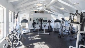 Ett gym med olika typer av träningsredskap, stora fönster och ett högt tak.