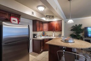 Una cocina con refrigerador de acero inoxidable, armarios de madera, una isla con encimera de granito, un fregadero y una planta en maceta.