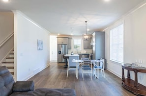 A spacious living area with a staircase, a dining table with chairs, a kitchen with a refrigerator, and a large window. - Nuttall Oak Retreat (Oxford)