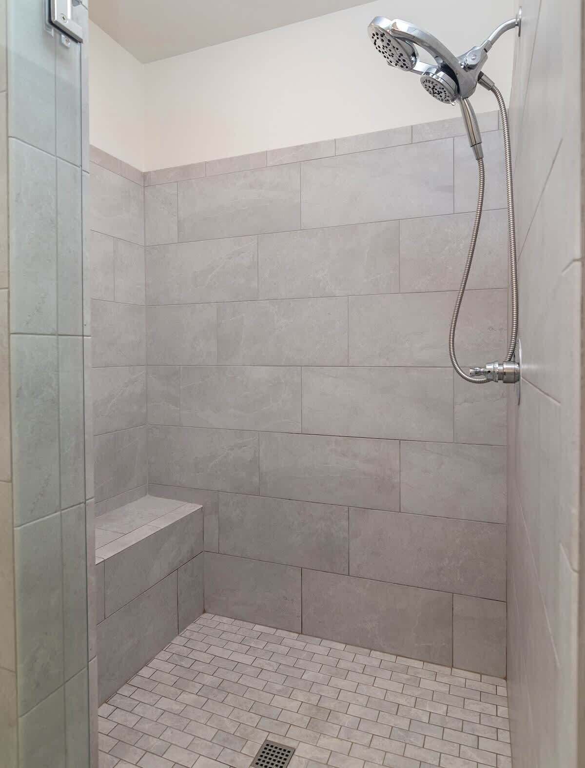 A shower with a handheld showerhead, tiled walls, and a brick-patterned floor.
