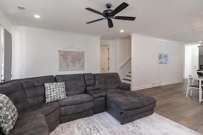 A modern living room with a sectional sofa, a ceiling fan, a world map on the wall, and a staircase leading to another level. - Nuttall Oak Retreat (Oxford)