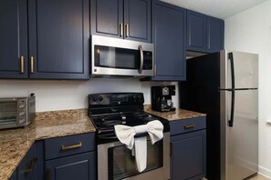 A kitchen with dark blue cabinets, stainless steel appliances, a granite countertop, and a towel hanging on the oven handle.