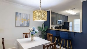 Un espace repas comprenant une table, des chaises, un luminaire suspendu, ainsi qu’un coin cuisine avec des placards, un four à micro-ondes et un réfrigérateur.