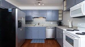 Una cocina con gabinetes grises, un refrigerador negro, un lavavajillas, una estufa y un microondas.