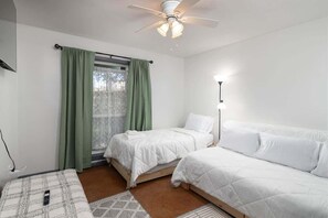 Une chambre avec deux lits, un ventilateur de plafond, une fenêtre avec des rideaux verts et une lampe de chevet.