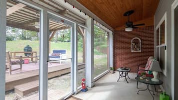 A covered patio with a wooden ceiling, large glass doors, a brick wall, and a ceiling fan.