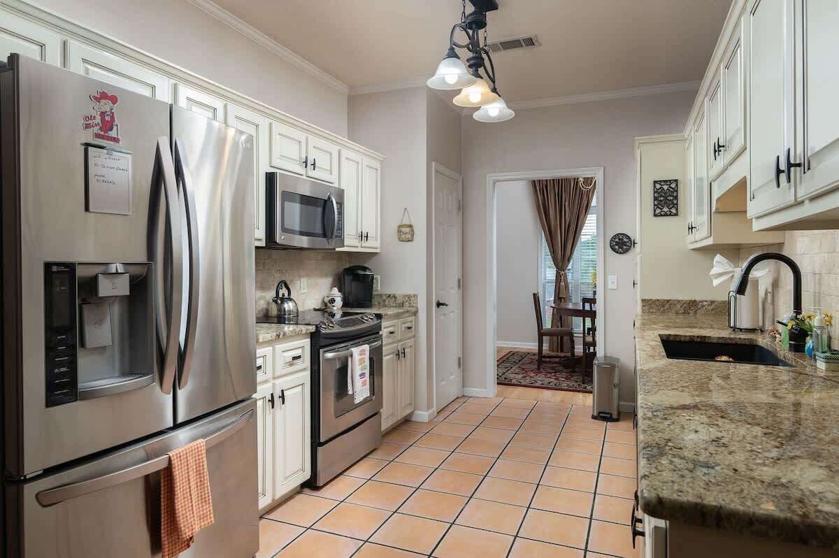 A kitchen with stainless steel appliances, white cabinets, a tiled floor, and a granite countertop.