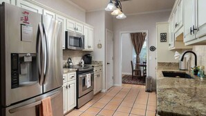 Una cocina con electrodomésticos de acero inoxidable, armarios blancos, piso de baldosas y encimera de granito.