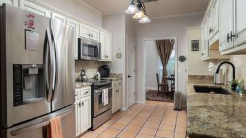 A kitchen with stainless steel appliances, white cabinets, a tiled floor, and a granite countertop.