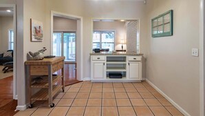 Una cocina con armarios blancos, encimera de madera, lámpara colgante y ventana con persianas.