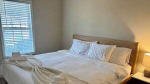 Un lit bien fait, avec du linge de lit et des serviettes blanches, une tête de lit en bois et une lampe de chevet.