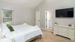 Ein Schlafzimmer mit einem Bett, einem Schminktisch, einem Fernseher und einer Tür.