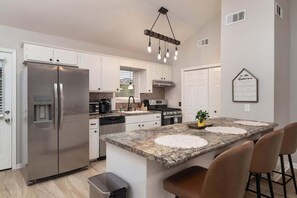 A modern kitchen with a stainless steel refrigerator, granite countertops, and a central island with bar stools. - Pet Friendly Rebel Retreat - Walk to stadium (Oxford)