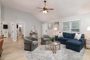 A living room with a ceiling fan, a blue sofa, a grey armchair, a coffee table, and a TV on the wall. - Pet Friendly Rebel Retreat - Walk to stadium (Oxford)