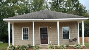 A single-story building with a gabled roof, a front porch with white columns, and a front door with a window above it. - Charming One - Bed Hideaway (Oxford)