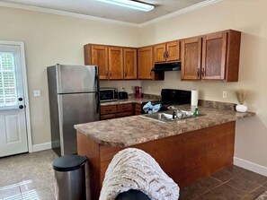 A kitchen with wooden cabinets, a stainless steel refrigerator, a granite countertop, and a trash can. - Charming One - Bed Hideaway (Oxford)