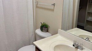 A bathroom with a toilet, sink, mirror, and shower curtain. - Charming One - Bed Hideaway (Oxford)