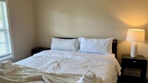 A hotel room with a bed, a nightstand with a lamp, and a window with blinds. - Charming One - Bed Hideaway (Oxford)