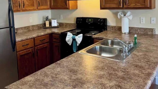 A kitchen with wooden cabinets, a stainless steel sink, a stove, and a refrigerator. - Charming One - Bed Hideaway (Oxford)