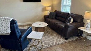 A living room with a sofa, a chair, a coffee table, and a TV mounted on the wall. - Charming One - Bed Hideaway (Oxford)