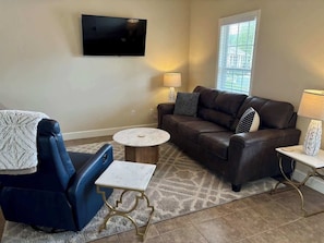 A living room with a sofa, a chair, a coffee table, and a TV mounted on the wall.