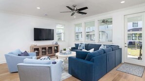 Ein modernes Wohnzimmer mit einem Ecksofa, einem Flachbildfernseher und einem Deckenventilator.
