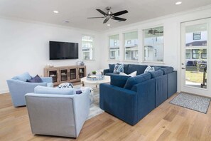 A modern living room with a sectional sofa, a flat-screen TV, and a ceiling fan. - Lily Loop Retreat (Oxford)
