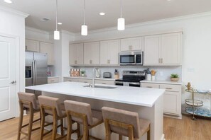 A modern kitchen with white cabinetry, stainless steel appliances, and a central island with bar stools. - Lily Loop Retreat (Oxford)