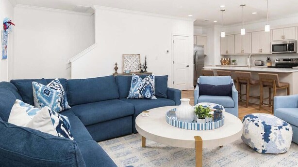 Ein modernes Wohnzimmer mit einem blauen Sofagarnitur, einem runden Couchtisch und einer Küche im Hintergrund.