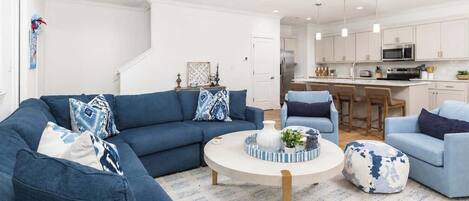 Un salon moderne avec un canapé bleu, une table basse ronde et une cuisine en arrière-plan.