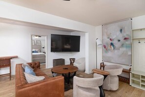 A modern living room with a sofa, round table, and chairs, a flat-screen TV, and a large abstract painting on the wall.