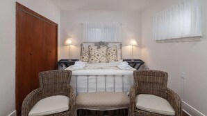 Ein Schlafzimmer mit einem Bett, zwei Nachttischen, einer Holztür, einem Deckenventilator und zwei Korbstühlen.