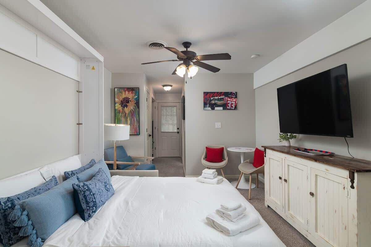 A hotel room with a bed, a TV, a ceiling fan, a desk, and a chair.