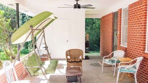 Eine überdachte Terrasse mit einer Schaukel, einem Korbstuhl und zwei weißen Stühlen.