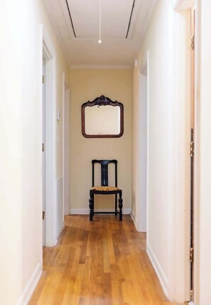 A hallway with wooden flooring, a chair, and a wall-mounted mirror.