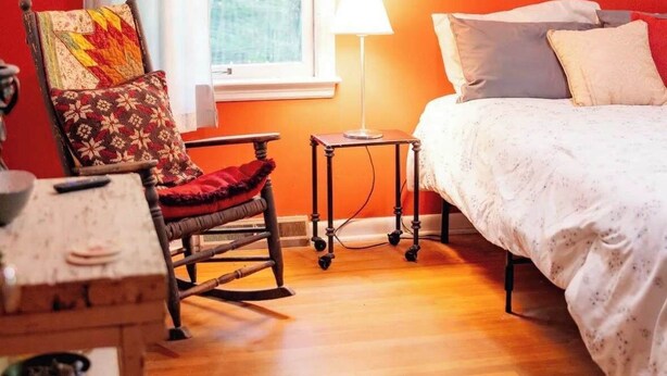 Ein Schlafzimmer mit einem Bett, einem Sessel mit einer Bettdecke, einer Lampe und einem Fenster.