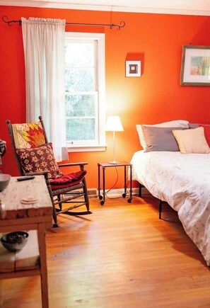Une chambre à coucher avec un lit, une chaise recouverte d’une courtepointe, une lampe et une fenêtre.