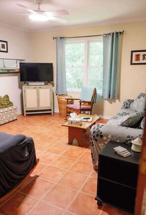 A living room with a television, a sofa, a chair, a small table, and a window with curtains.
