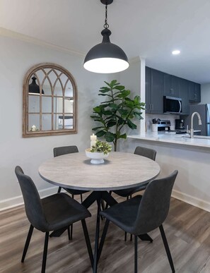 A modern kitchen with dark cabinets, a round dining table, and a hanging pendant light. - Victory Retreat (Oxford)