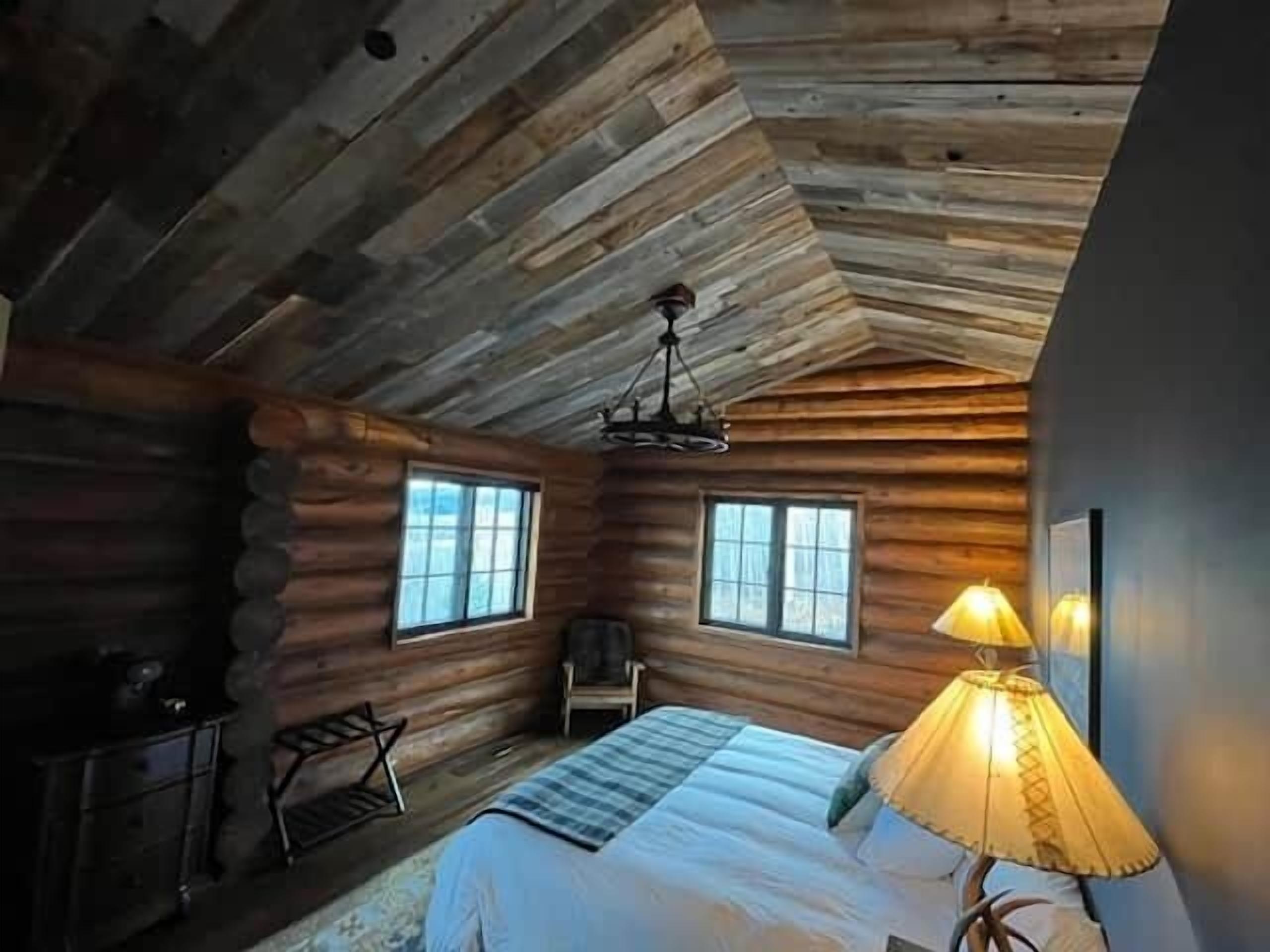 Quarto de cabana de tronco com uma cama, uma cadeira e um abajur.